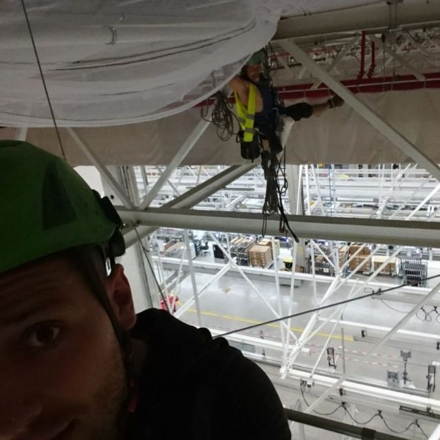 Rigging-Techniker an Traversen über einer Logistikhalle
