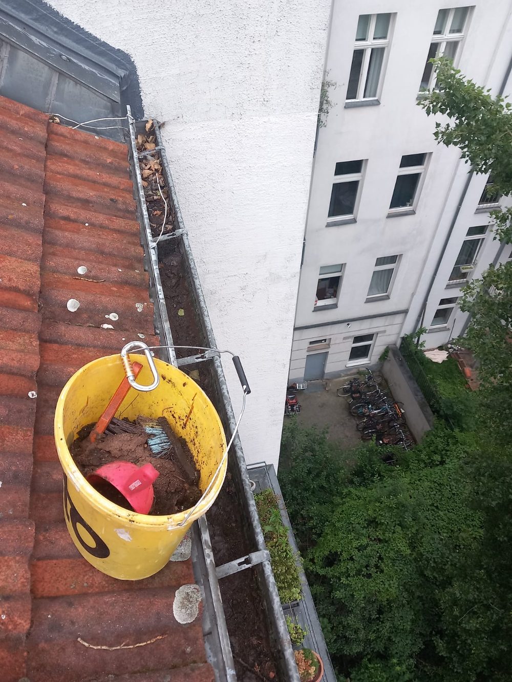 Bucket of gutter debris hanging at height during cleaning