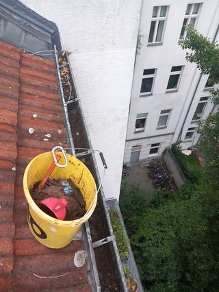Bucket of gutter debris hanging at height during cleaning