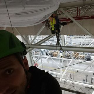 Rigging technicians working overhead trusses inside a logistics facility
